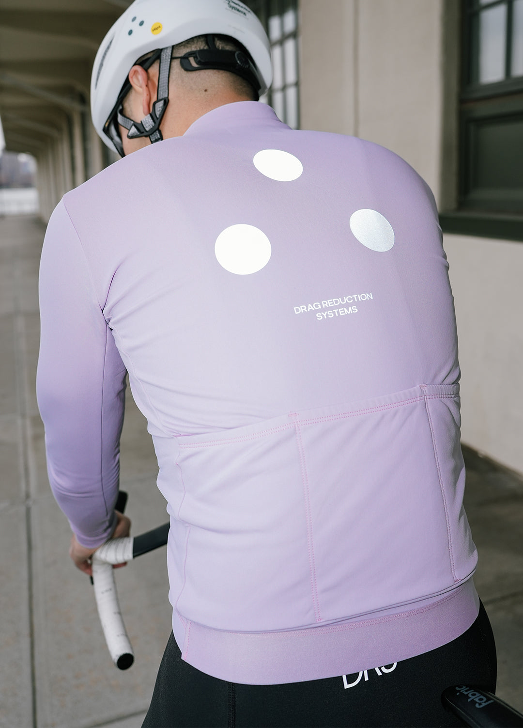 Person wearing a light purple cycling jersey with reflective elements and a helmet in Brooklyn, New York.