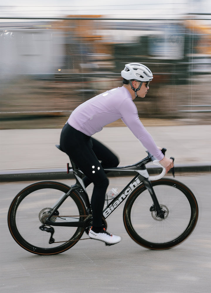 Person riding a bicycle on a Brooklym road wearing DRS cycling jersey and bibs with a blurred background. 