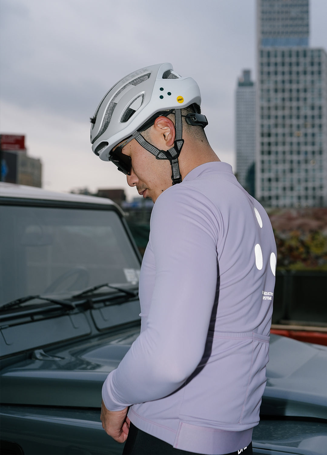 Cyclist wearing a helmet and light purple DRS cycling outfit with NYC cityscape background