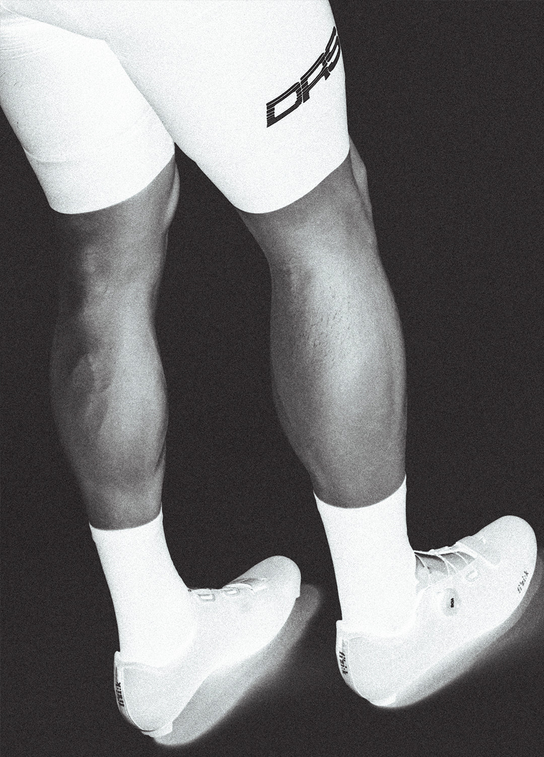 Black and white image of a person wearing white socks with a DRS cycling bib on a black background.