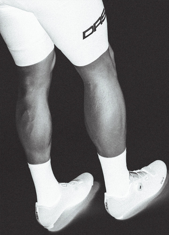 Black and white image of a person wearing white socks with a DRS cycling bib on a black background.