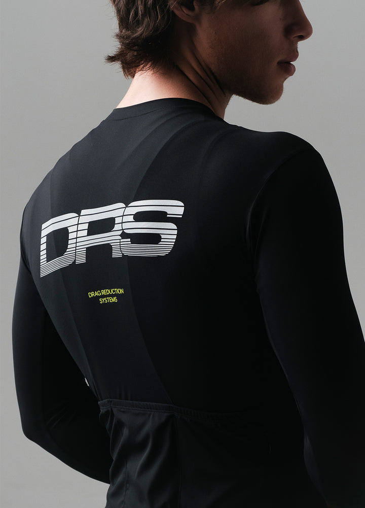 Person wearing a black long-sleeve cycling jersey with 'DRS' branding on the back against a gray background