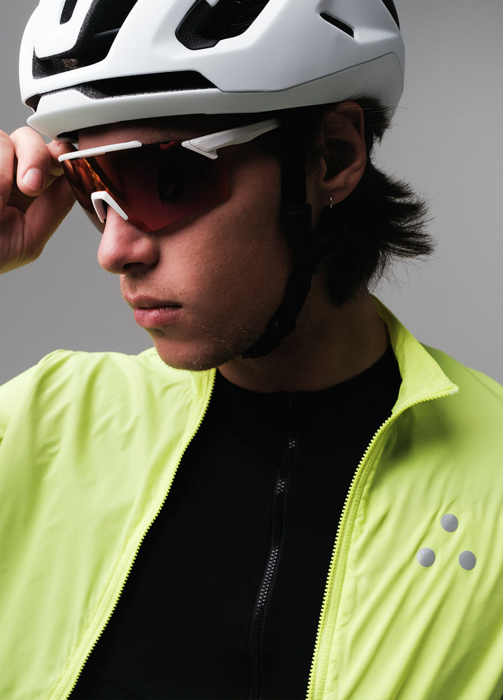 Person wearing a white helmet and bright yellow DRS cycling jacket with sunglasses, on a gray background