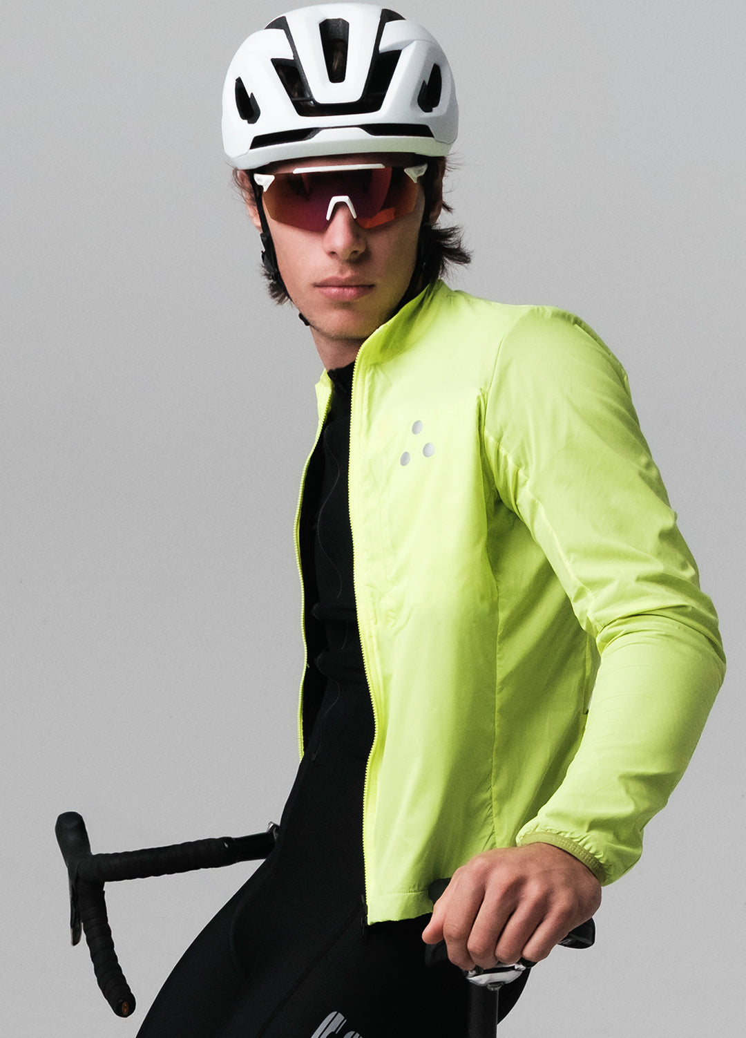 Person wearing a bright yellow DRS cycling jacket, helmet, and sunglasses, holding a bicycle on a gray background.