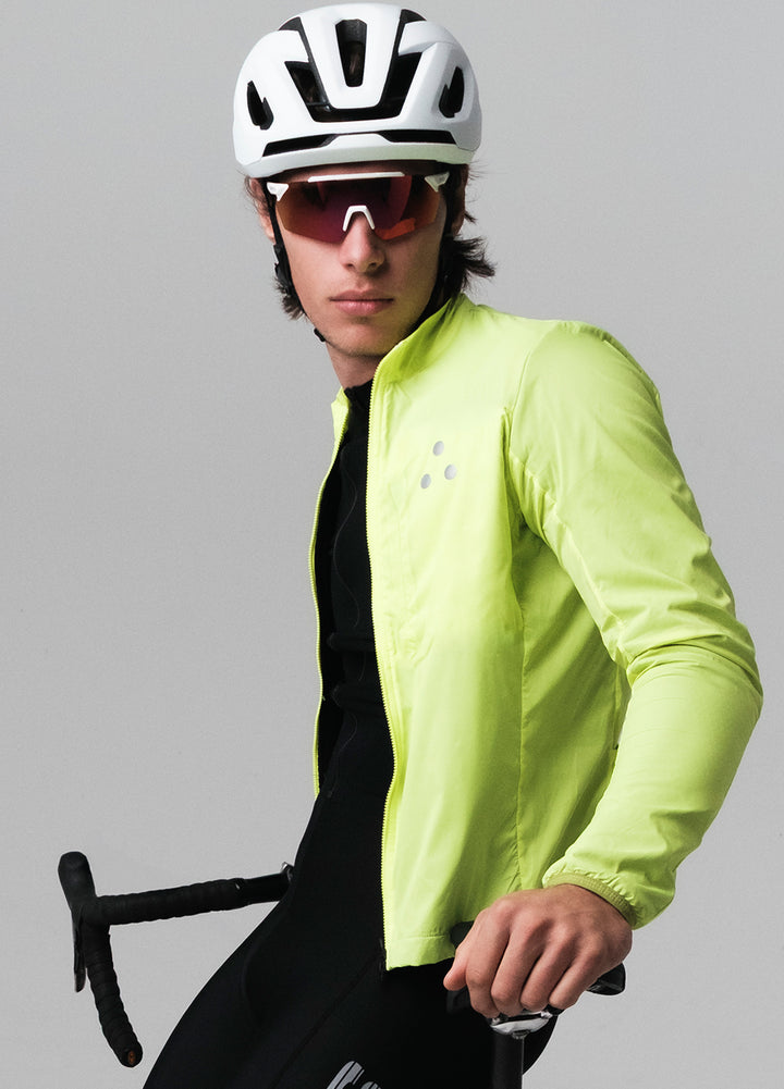 Person wearing a bright yellow DRS cycling jacket, helmet, and sunglasses, holding a bicycle on a gray background.