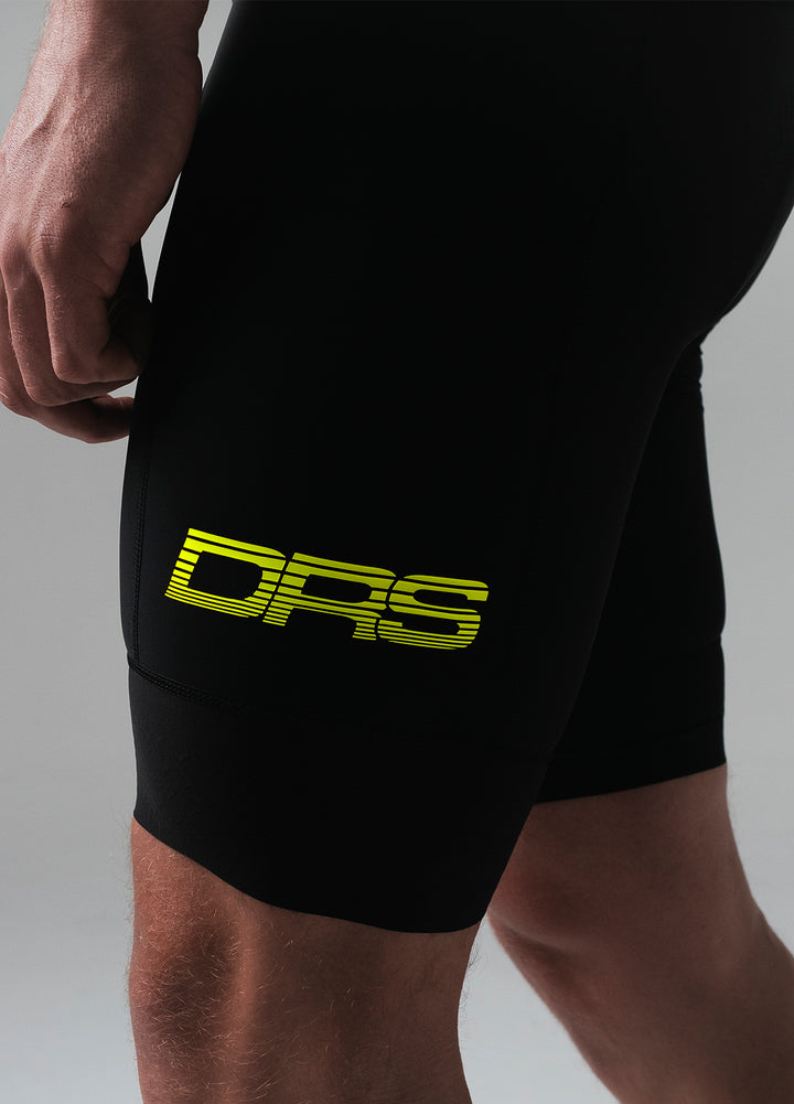 Black DRS cycling bib shorts with a yellow labs logo on a gray background
